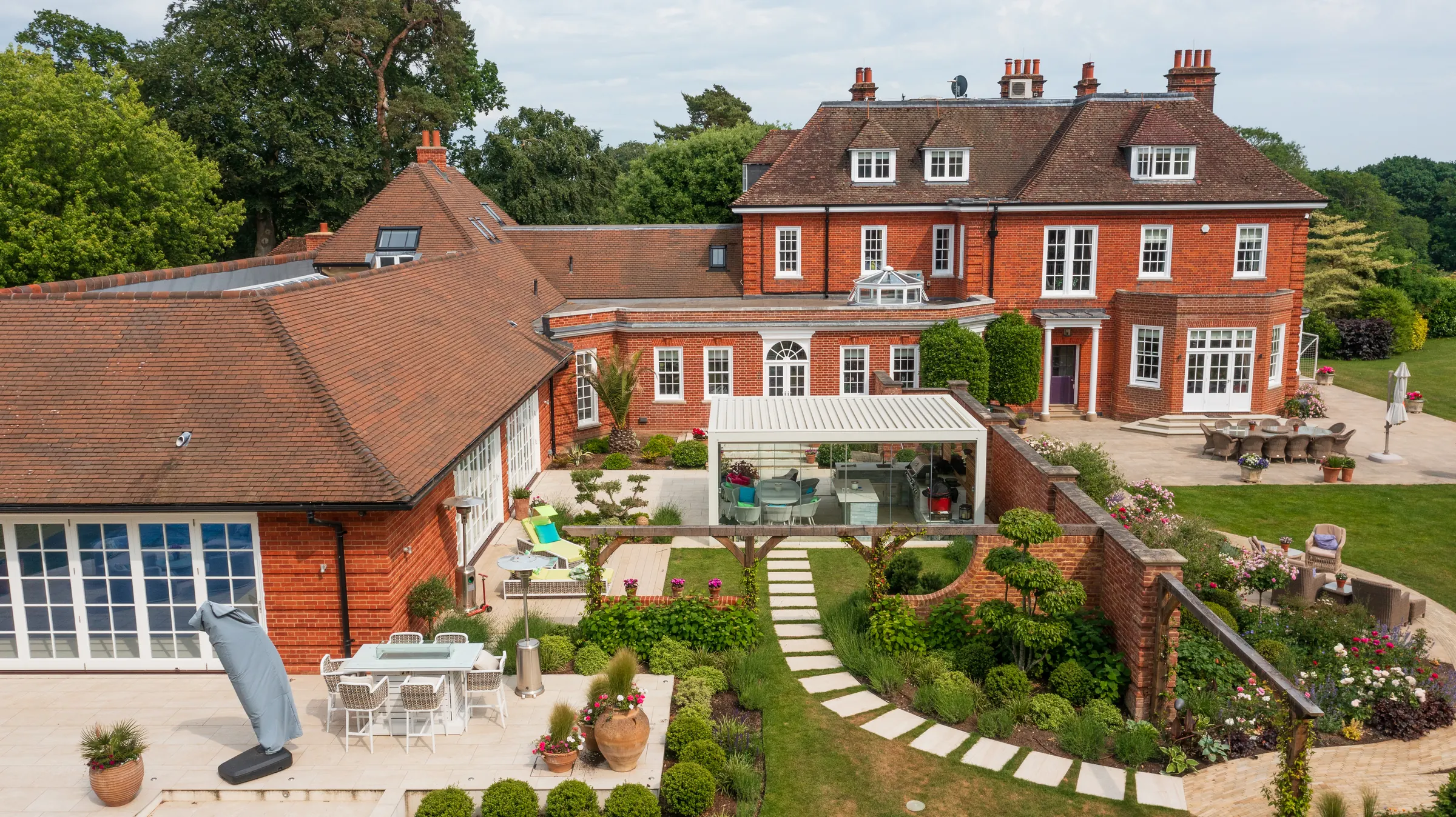 A red-brick country house and its gardens, pool house and grounds, seen from the air