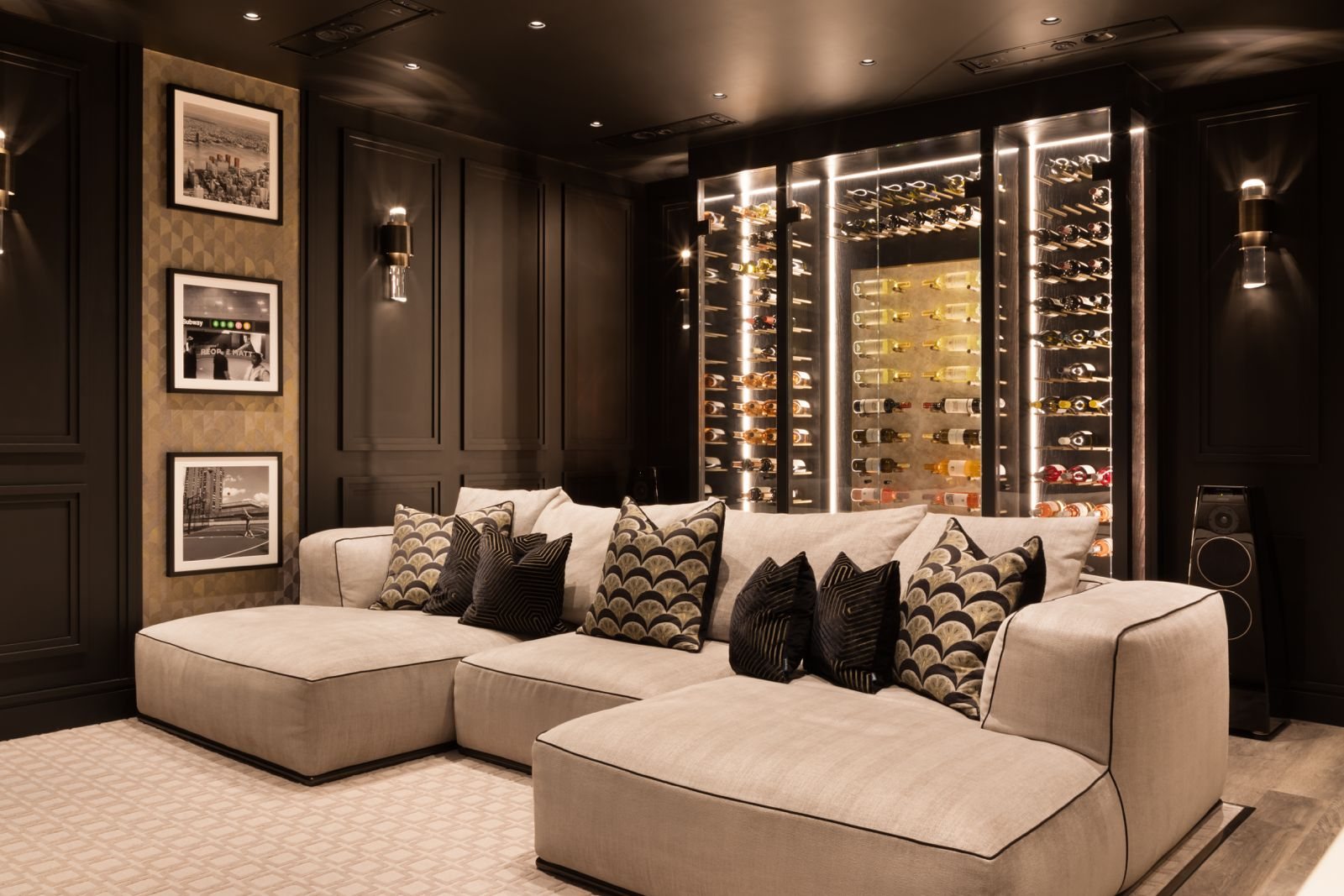A media lounge with a deep sectional sofa in front of the illuminated wine wall